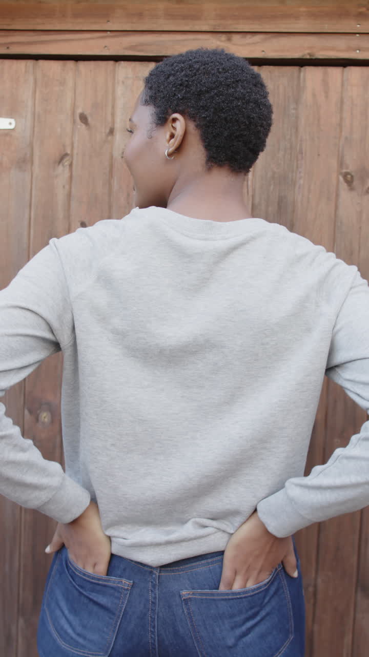 Vertical video of rear view of african american woman in grey sweatshirt with hands in back pockets