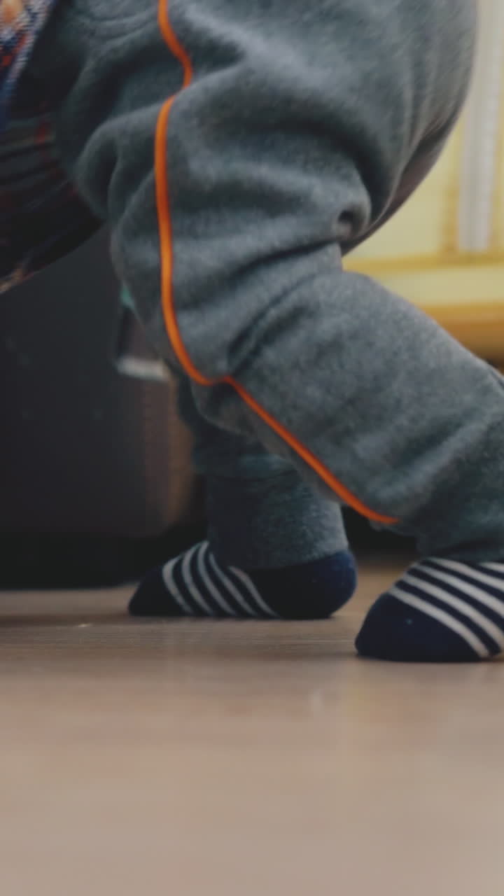 funny small baby in grey pants plays at large bed on wooden floor in children room close backside view