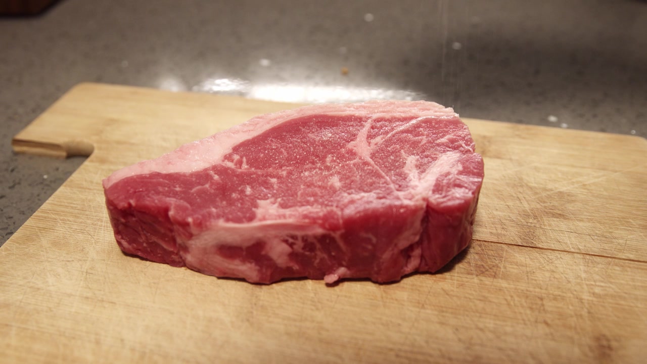 Seasoning a fresh beef steak with salt and pepper. Pouring salt and pepper on meat