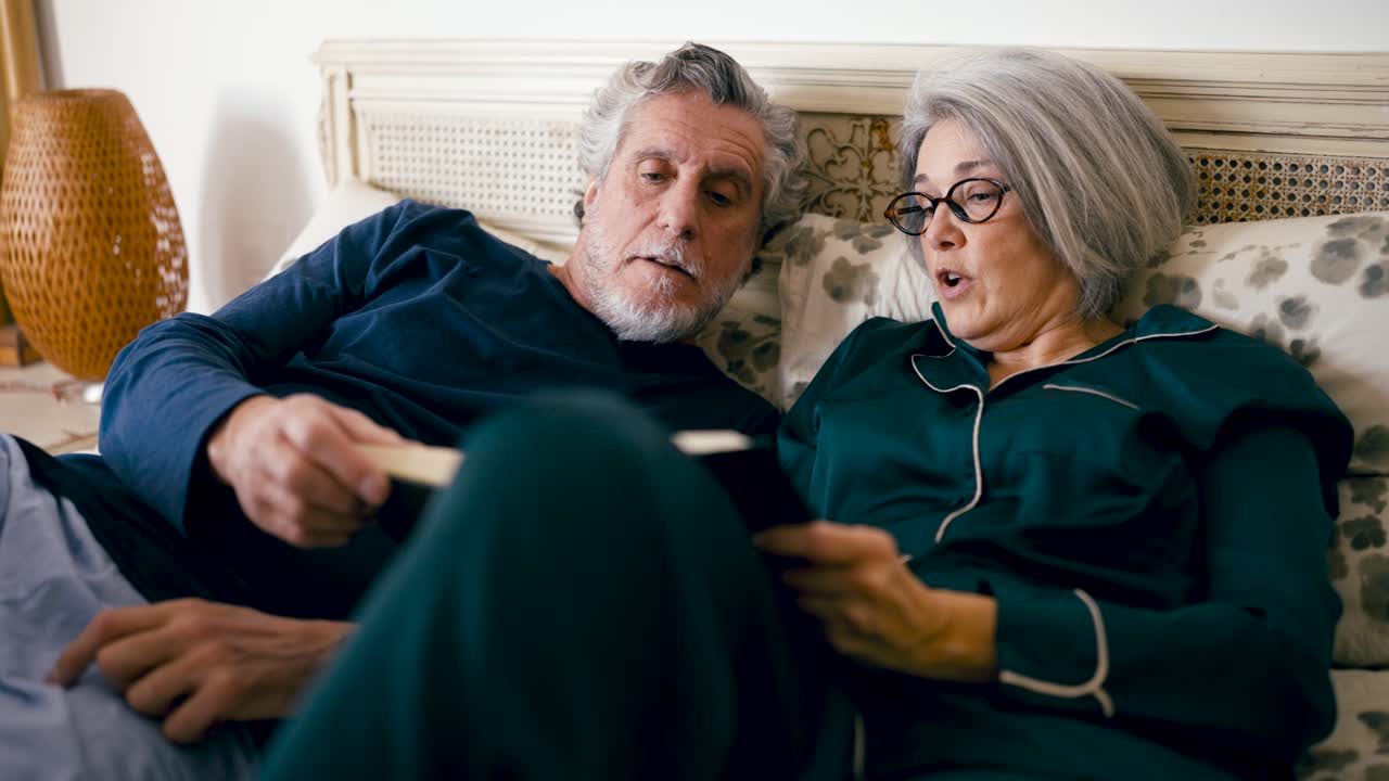 Pareja de ancianos leyendo y hablando en la cama