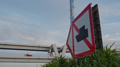 a close-up shot of a prominent junction warning sign with an elevated highway and cloudy sky in the background
