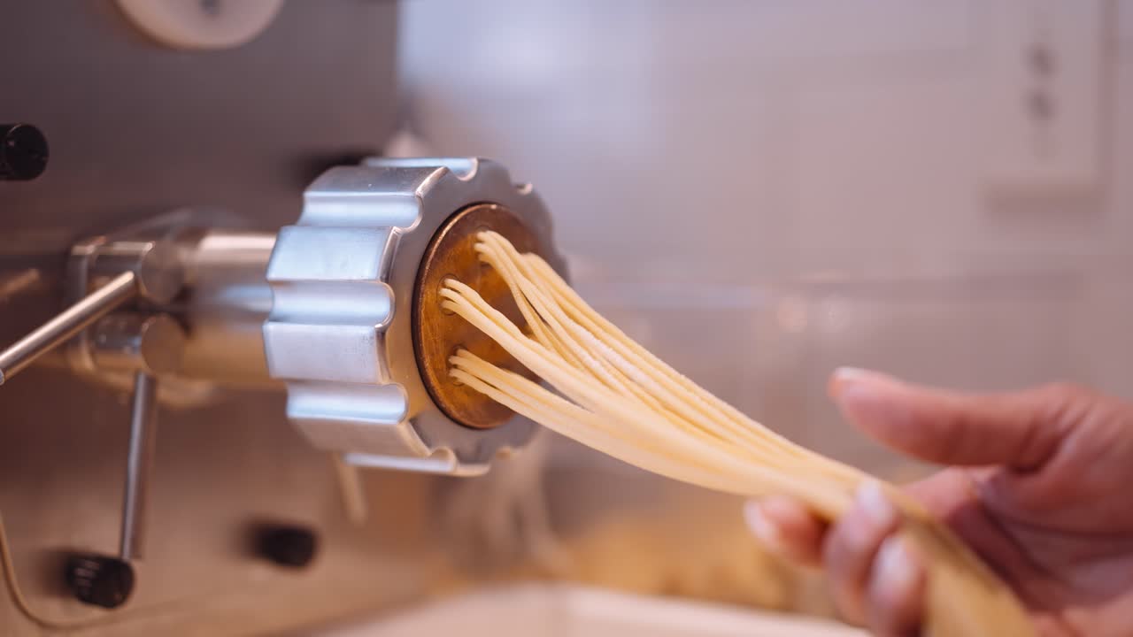 el cocinero masculino acompaña las largas hebras de espagueti de la máquina de pasta