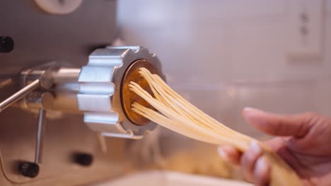 male cook accompany the long strands of spaghetti from the pasta machine