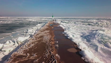 man and woman standing near a lighthouse at the end of a dock overlooking a frozen blue lake