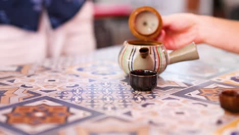 A serene tea pouring ritual with a striped teapot on a patterned table, highlighting cultural elegance and precision