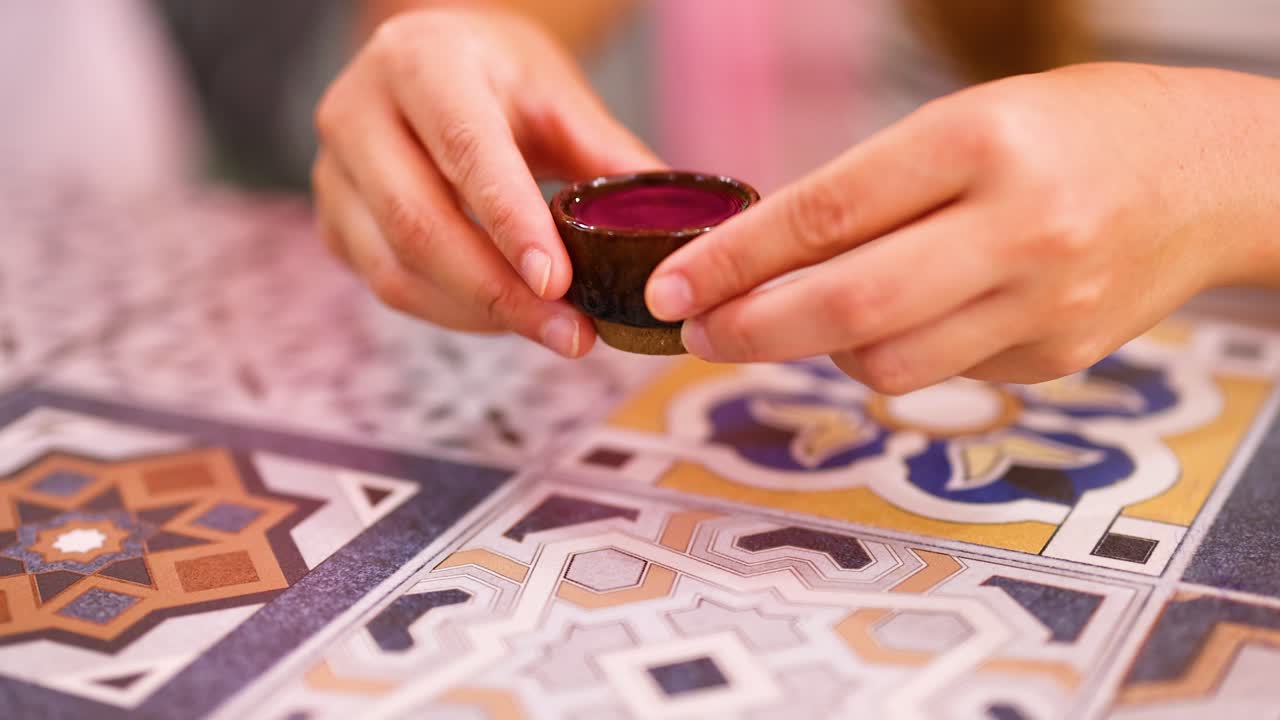 las manos manejan suavemente una taza pequeña en una mesa de colores y patrones, creando una atmósfera cálida e íntima con una iluminación suave