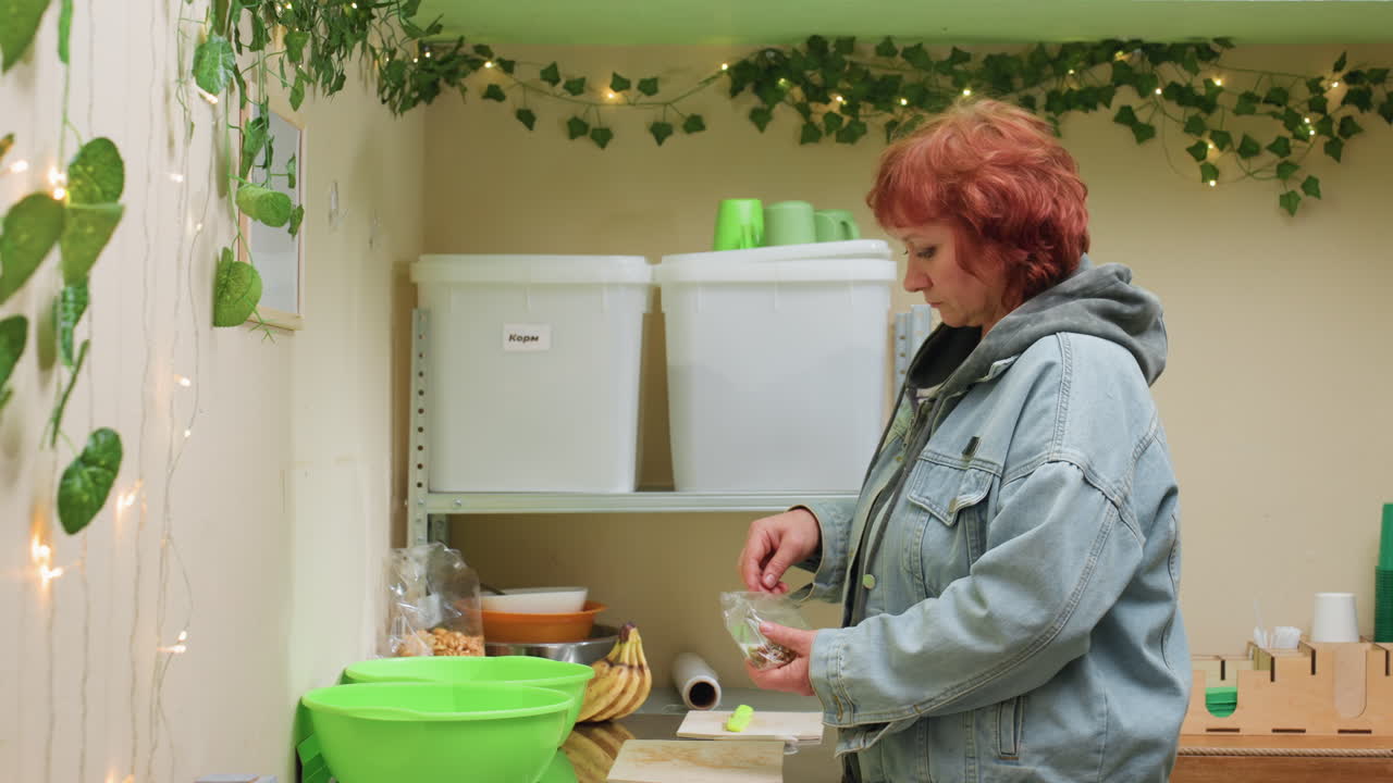 Hvit kvinne forbereder kompost med bananskall over et grønt basseng, iført dongerijakke, sorterer matrester på benken nær glass og beholdere, innendørs planter og lyslenker skaper en koselig øko-atmosfære