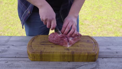 hands cutting meat using a knife on a wooden surface outside