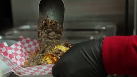 adding marinated, chopped steak to fries and cheese to make carne asada fries - food truck series