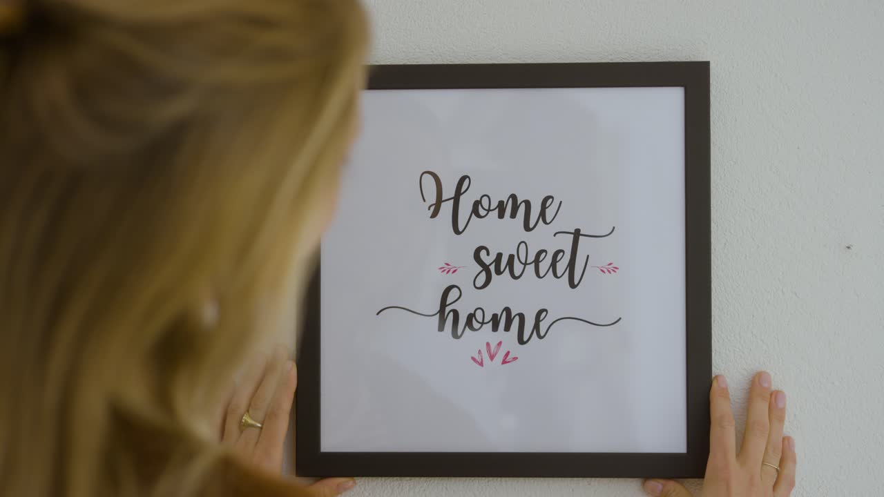 mujer colgando el marco "hogar dulce hogar" en la pared