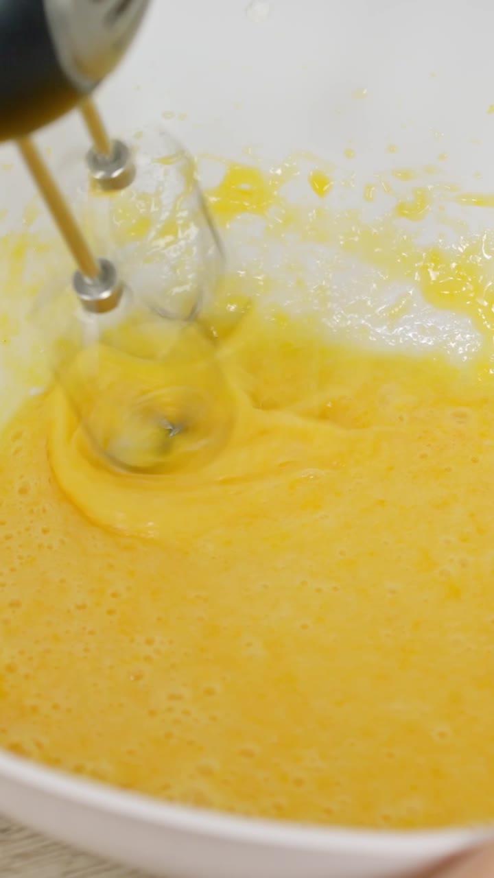 Close-up of thick yellow custard being mixed using electric hand mixer in tiramisu prep, vertical