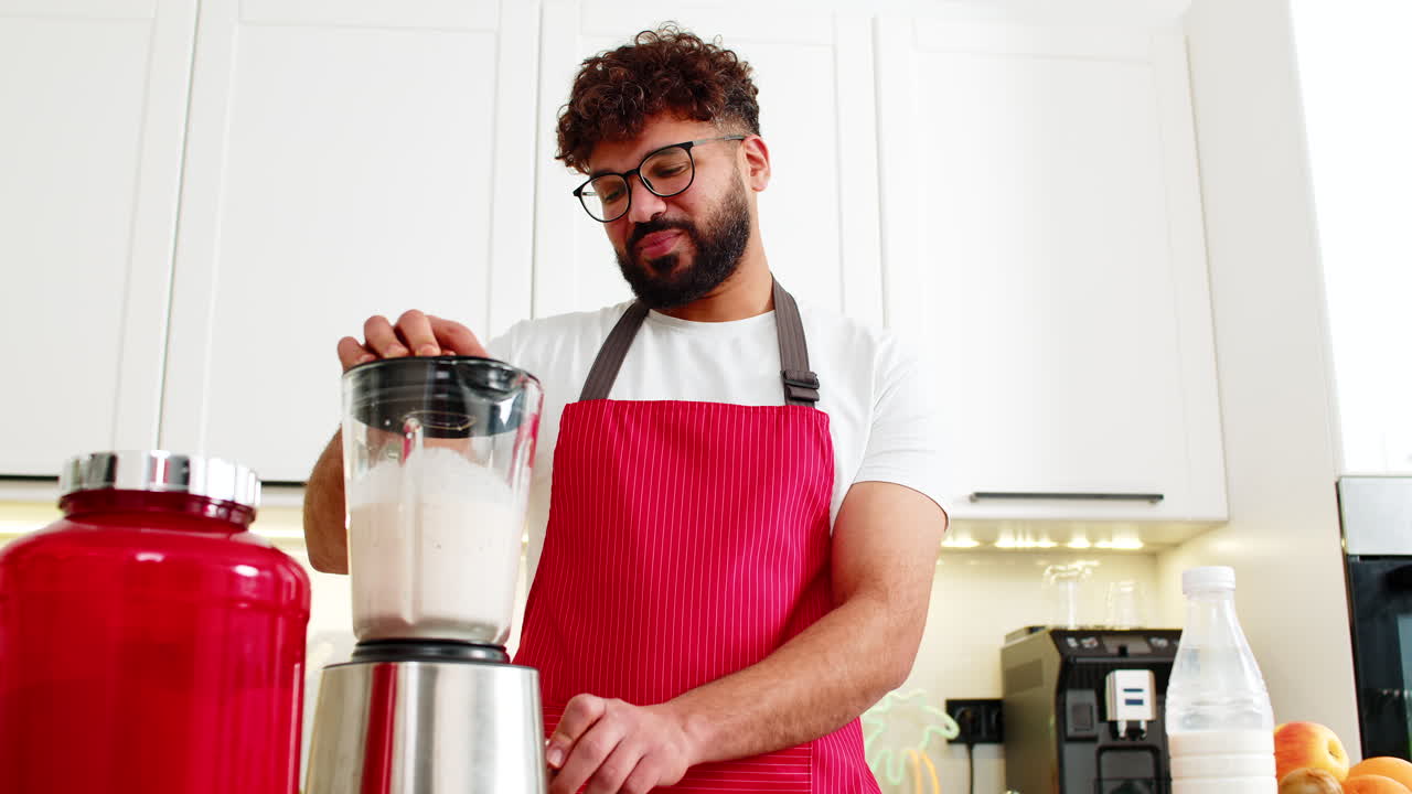 Giovane adulto arabo che frulla un frullato di proteine del siero del latte nella cucina di casa per una sana alimentazione fitness