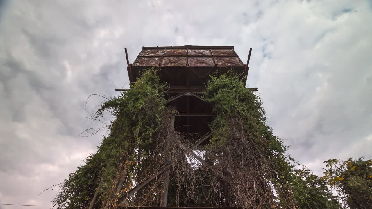 A motion control time-lapse of an old water storage tower overgrown with plants and fast-moving cloud cover