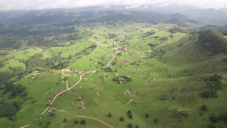 Sirnea-village-in-romania-with-scattered-houses,-lush-green-fields,-and-cloudy-sky,-aerial-view