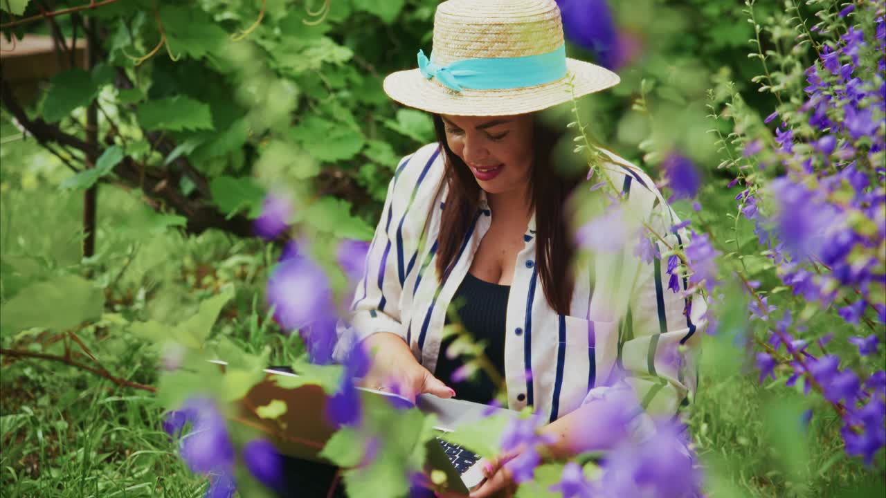 Woman in straw hat enjoying nature while reading a book surrounded by vibrant flowers in garden