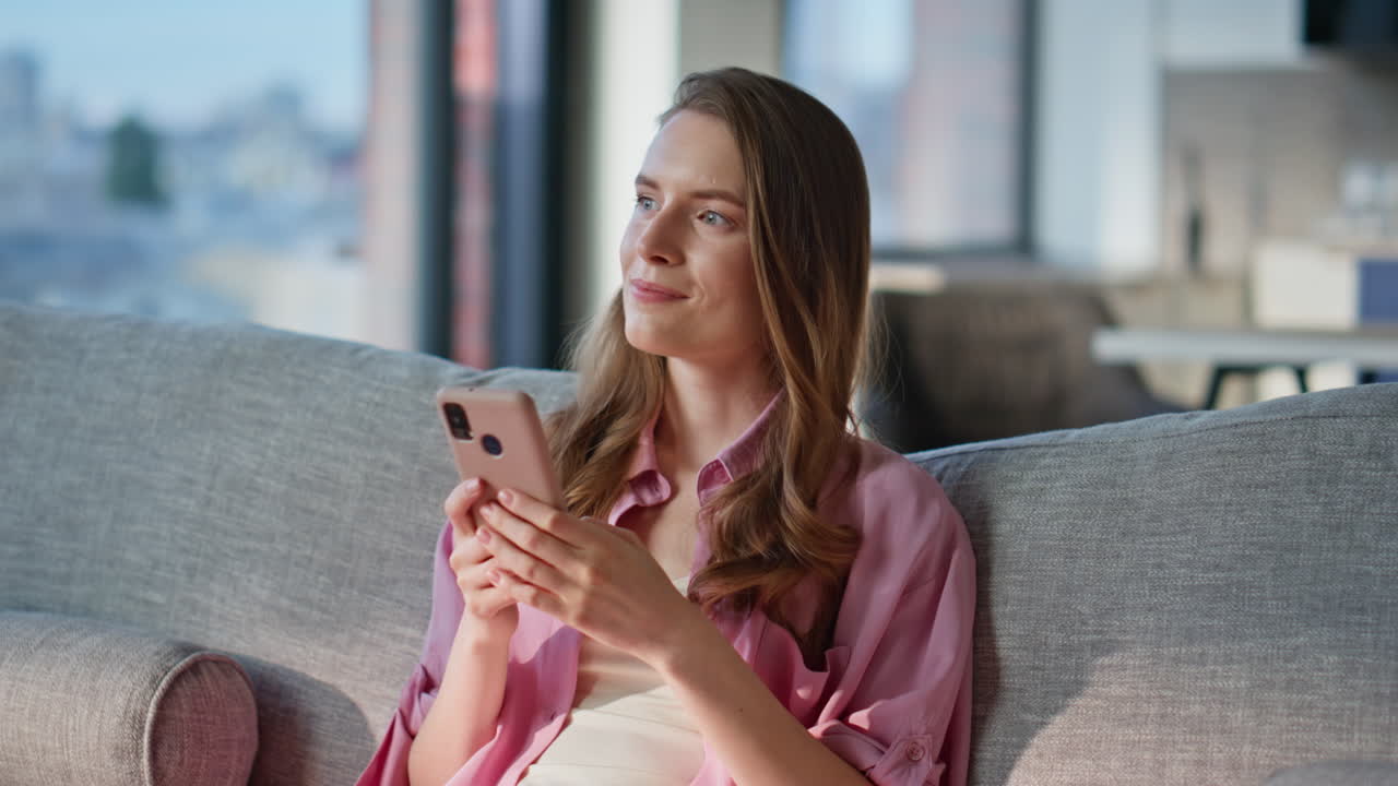Smiling woman using mobile phone sitting sofa in relaxed home setting ...