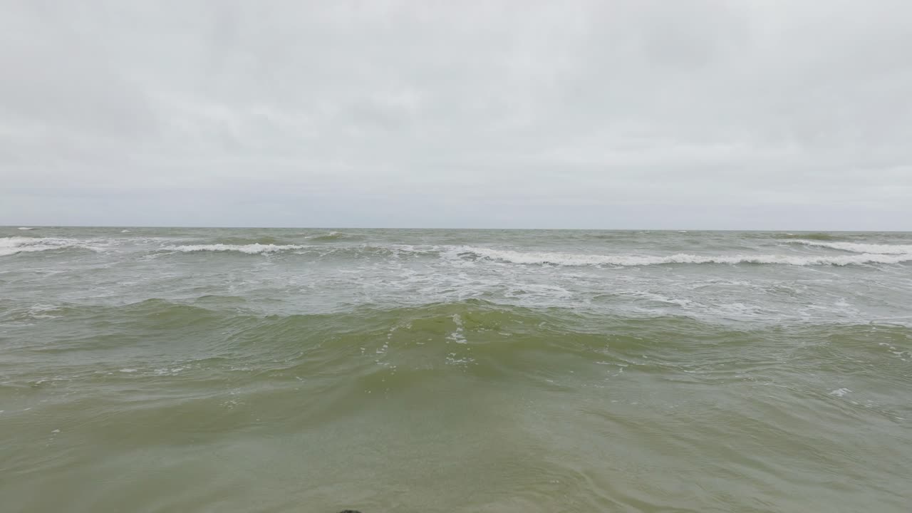 흐린 날 발트해 연안의 공중 전망, 오래된 목조 부두, 하얀 모래 해변, 해안에 부딪히는 큰 폭풍우, 기후 변화, 넓은 드론 샷이 뒤로 낮게 움직입니다.