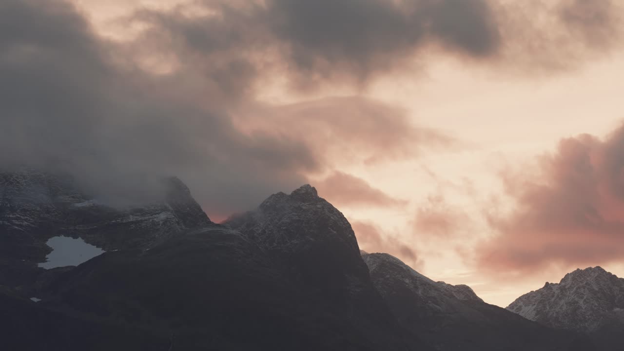 nubes tormentosas iluminadas por el sol poniente pasan por encima de las cimas de las montañas cubiertas de nieve