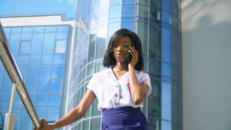 adult african american young businesswoman is talking on phone outside near modern office building