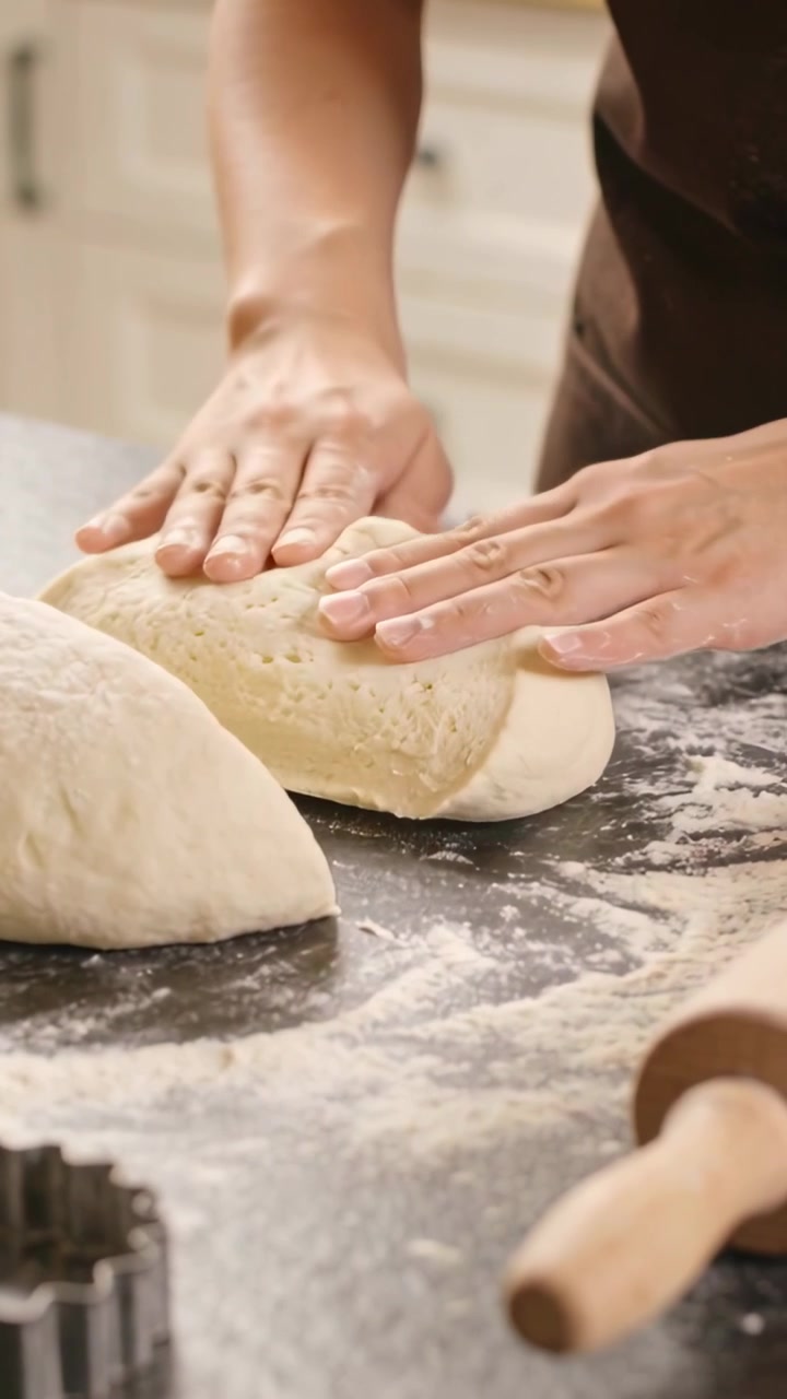 Vertical video: Lifting dough, hands shaping into loaves on floured counter in apron, pin nearby