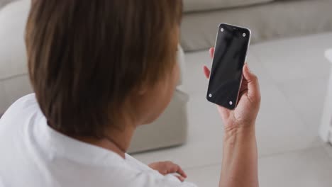 mujer mayor afroamericana sentada en el sofá usando un teléfono inteligente, con espacio de copia en la pantalla