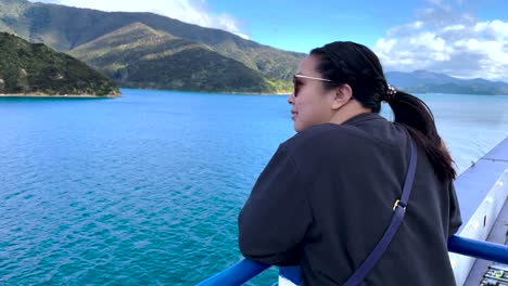 over the shoulder view of asian woman looking at tree covered islands and water from a boat in new zealand