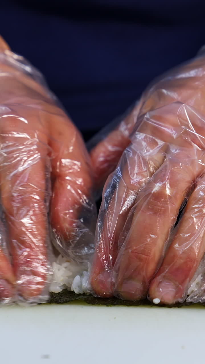 Chef in gloves is preparing sushi. Sushi are made of rice, nori seaweed, cucumber, cream cheese. Appetizing and nutritious food concept. Vertical video
