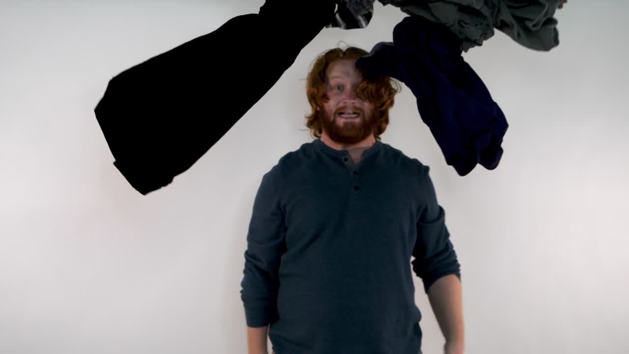 A young red-haired man having laundry falling on his head with an anxious look on his face