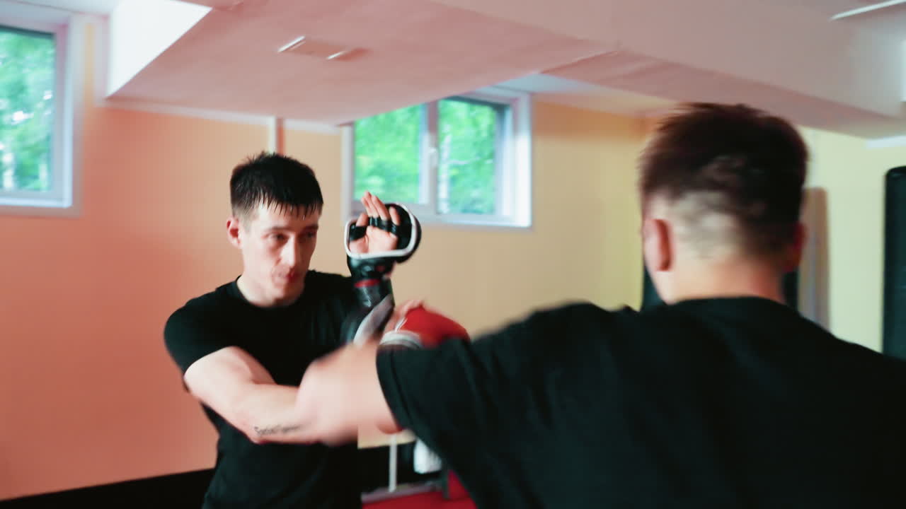 Fighters preparing for sparring session inside gym, fighting ready with black gloves facing opponent in black shirt, showing determination, focus, combat mindset, and readiness for boxing training