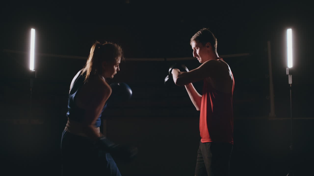 hermosa boxeadora morena trabajando golpes a las patas con un entrenador en una habitación oscura