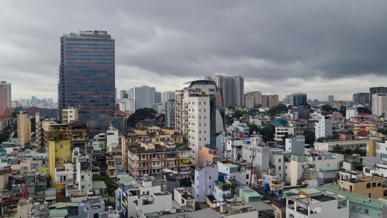 High-rise view over rooftops of District 1, Ho Chi Minh City, Vietnam, under a moody monsoon sky, capturing the layered urban landscape and vibrant architectural colors of the capital