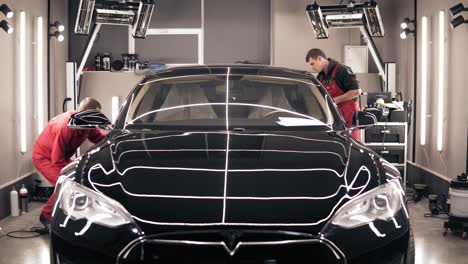 odessa, ukraine - december 06, 2017 two professional workers polish new black tesla car from both sides. making it look extra-shiny.