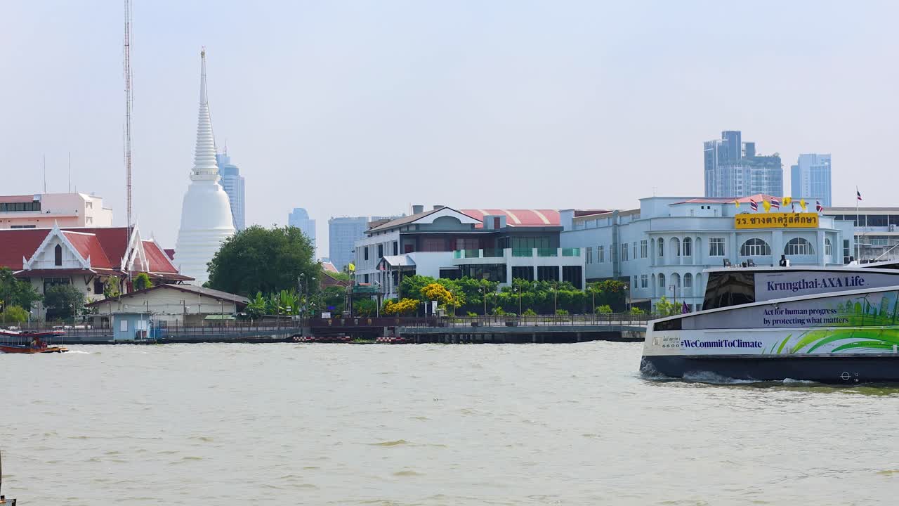 An electric ferry glides across the Chao Phraya River in Bangkok, showcasing urban architecture and serene waterway under bright daylight