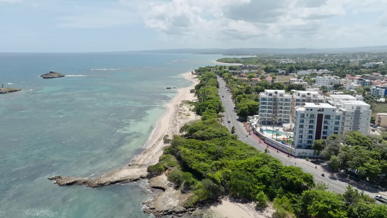 Puerto Plata coastline, sandy beach, coastal road, and city buildings, Dominican Republic. Aerial forward