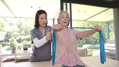 assisting senior asian woman with resistance band exercises, physical therapist at home