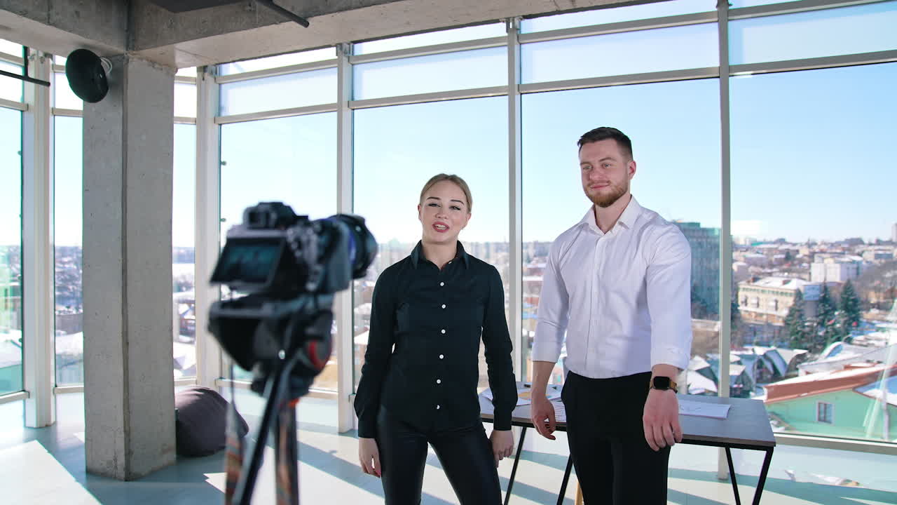 Young couple shooting video about their business. Beautiful woman and handsome guy standing in front of professional camera and talking for video in the studio.