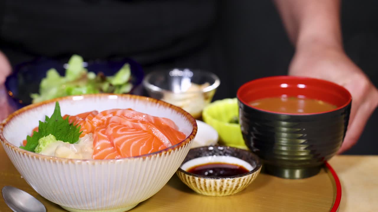 Un cameriere appoggia una ciotola di donburi con sashimi di salmone fresco su un vassoio tradizionale giapponese.
