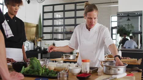 caucasian female chef teaching diverse group preparing dishes and smiling