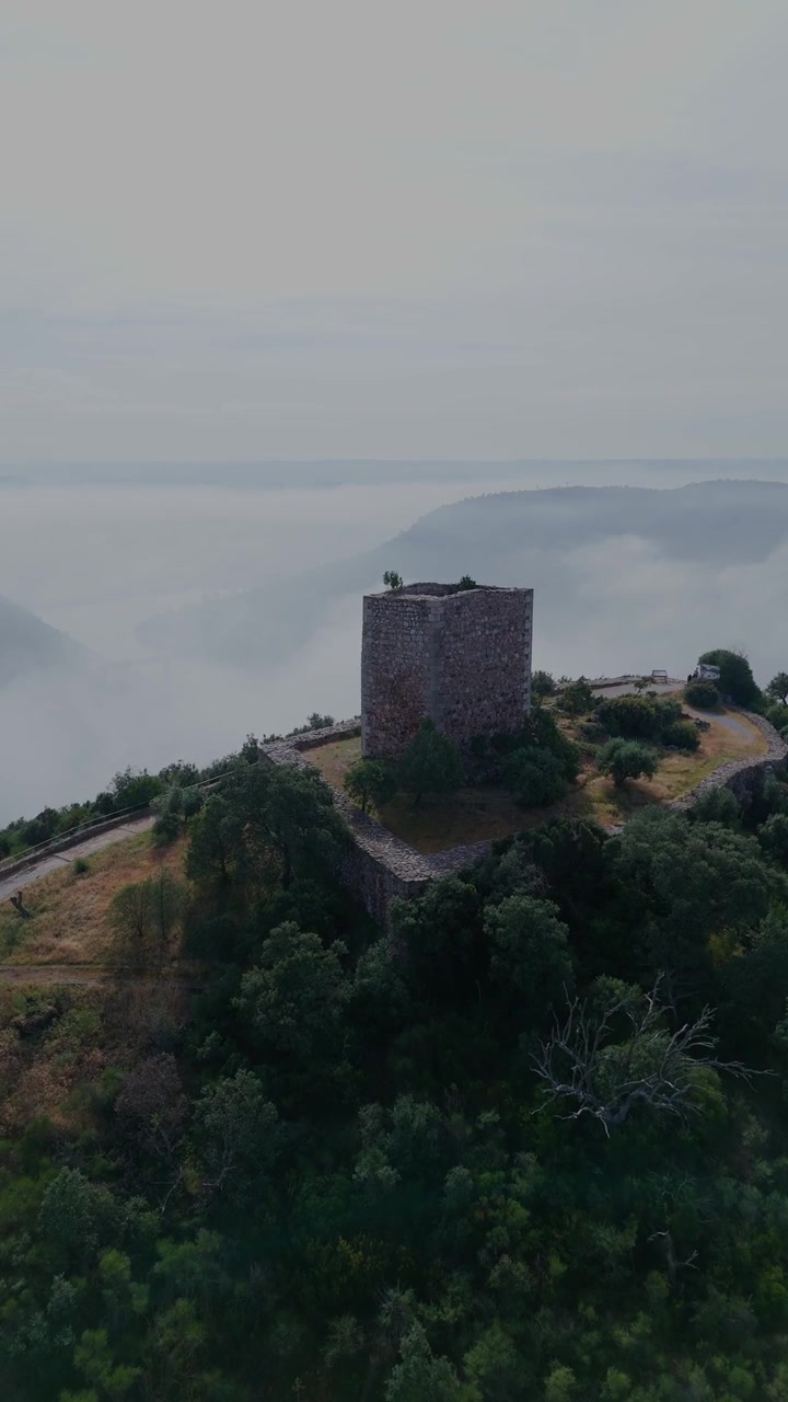 Ripresa verticale con drone che avanza e scende sopra il Castelo de Rodao, rivelando la cappella, il fiume Tago, il paesaggio circostante e la nebbia mattutina.