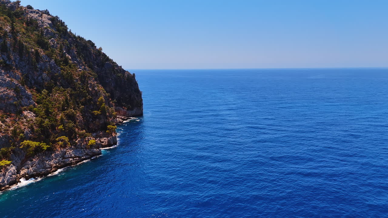 Serene coastline meets clear blue ocean. A stunning view of a rugged coastline extending into the calm blue ocean on a clear day, capturing nature's beauty