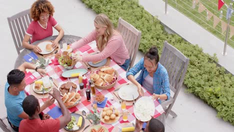 Fröhliche,-Vielfältige-Gruppe-Von-Freunden,-Die-Am-Esstisch-Im-Garten-Essen-Und-Reden,-Zeitlupe