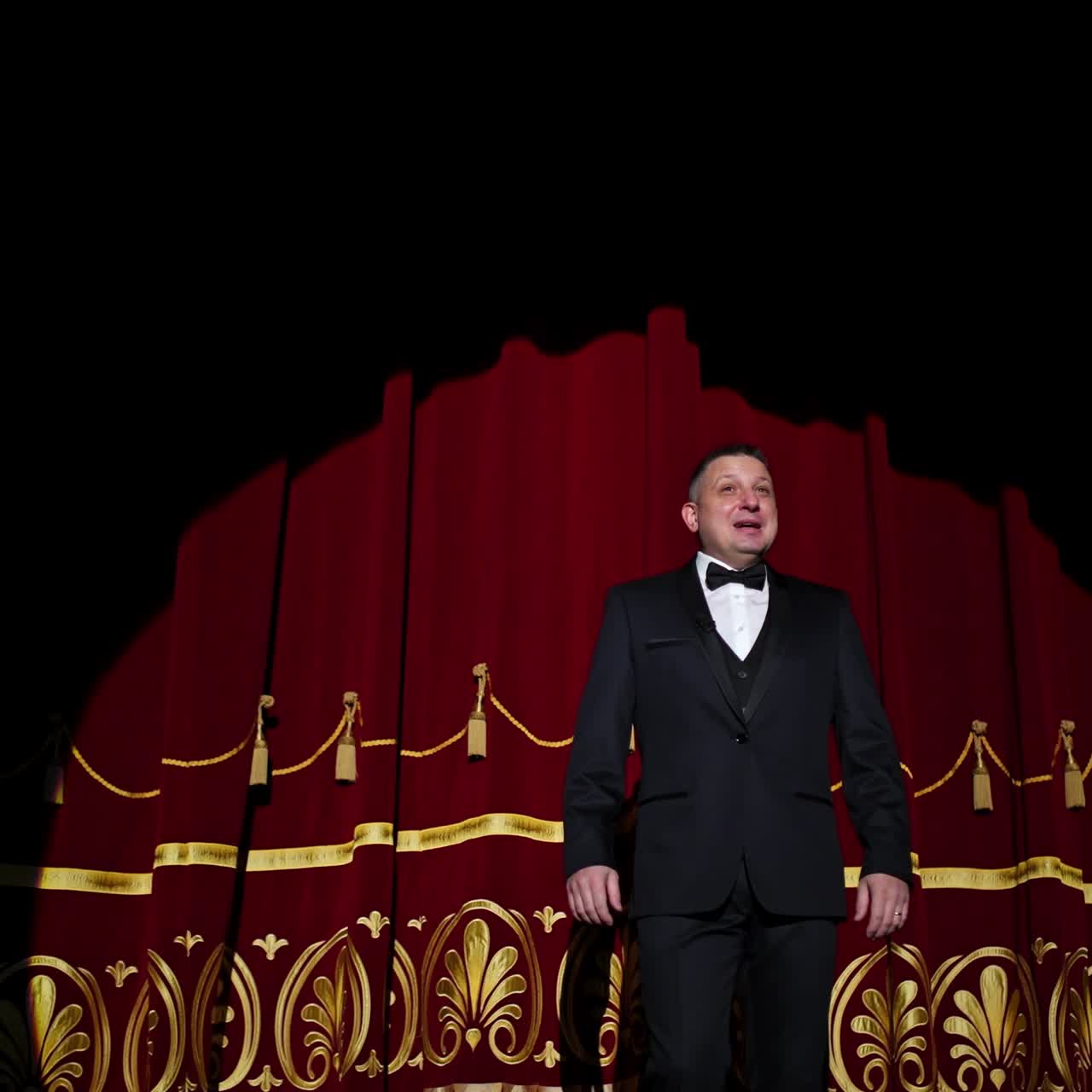 Theatrical stage. Man in costume appearing on a scene and presents the performance in light spot on dark background