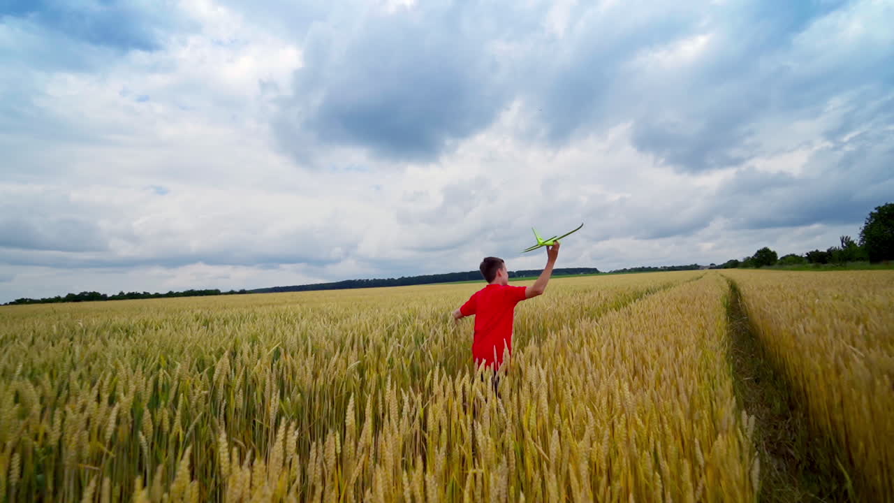 Boy launching toy plane in the field. Teenager runs with plane on yellow field under blue sky. Happy child playing in summer nature.