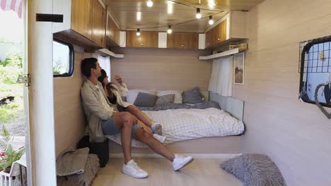 well designed wheels house - smiling optimistic couple man and woman smiling while hugging in trailer mobile home, sitting on