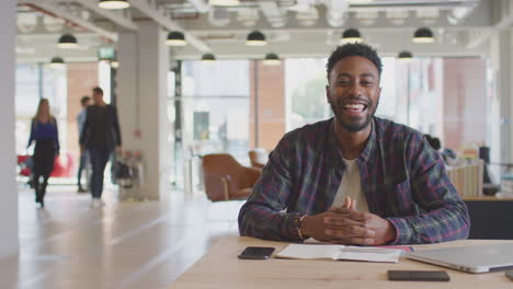 portrait of businessman working at desk in modern open plan office with colleagues in background