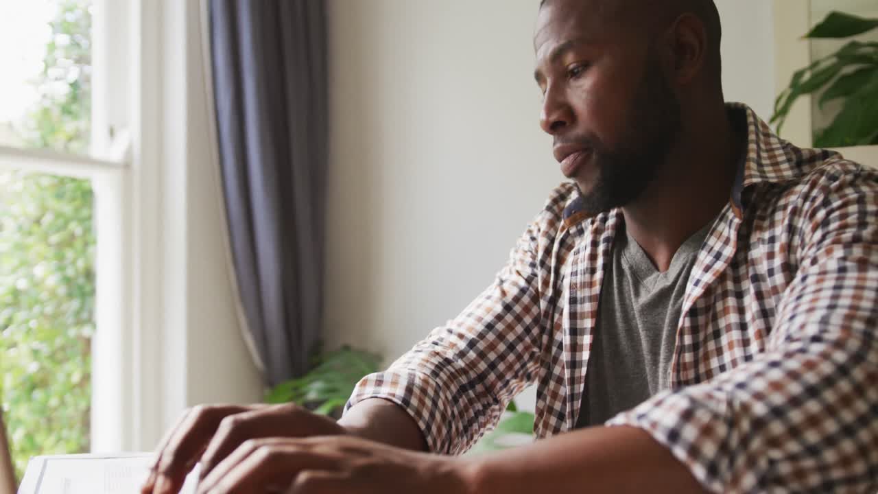 African american man working at home sitting at table using laptop
