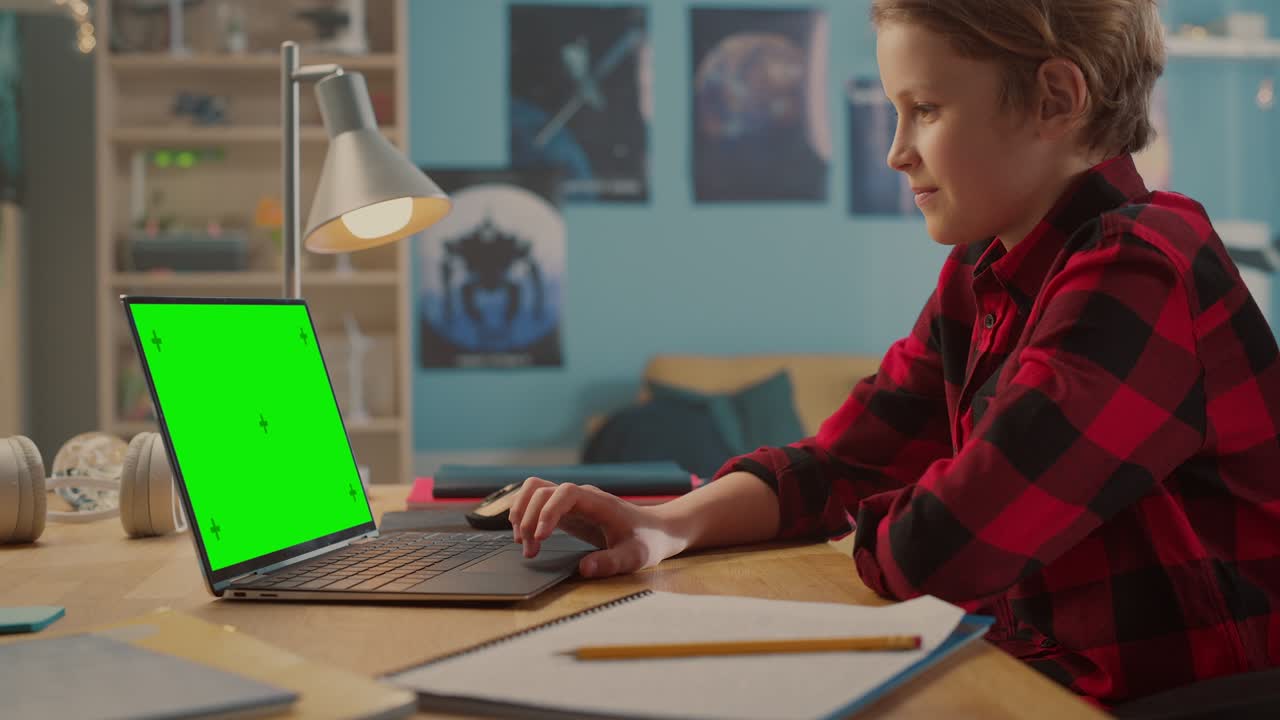 Smart Young Boy Researching Homework on Laptop Computer with Green Chroma Key Screen Display Mock Up. Teenager Browsing Educational Research, Chatting on Social Media, Studying School Material.