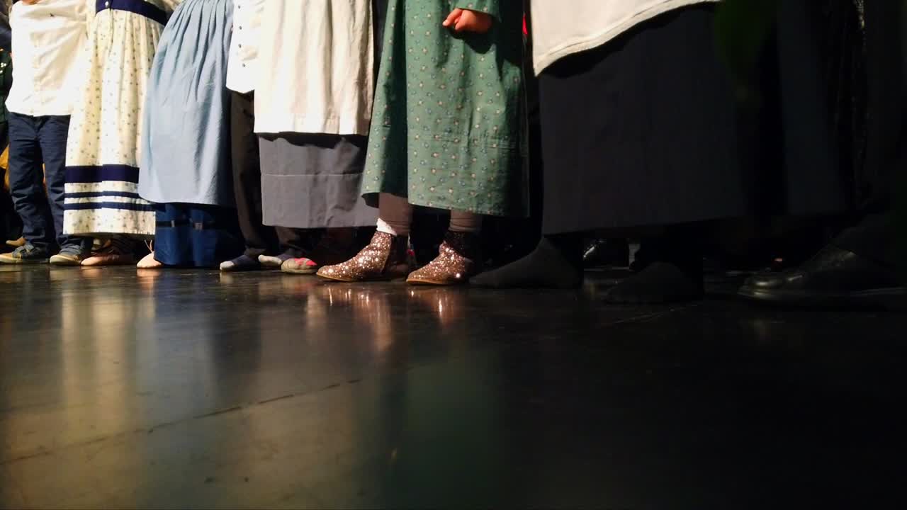 grupo de personas que usan vestidos largos tradicionales mientras golpean los pies y se mueven