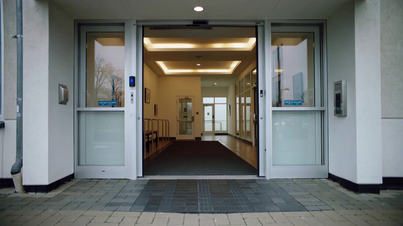 Opening sliding glass doors after motion sensor activation at main entry, revealing lobby seating
