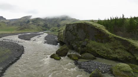 a peaceful river winding through a rocky landscape in hafursey, iceland, with green hills and mist-covered mountains in the background.